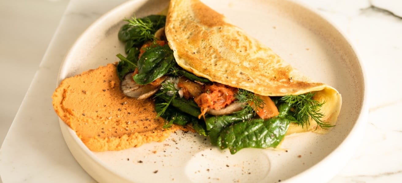 An omelette sitting on a plate, inside the omelette is various herbs and an unknown protein.